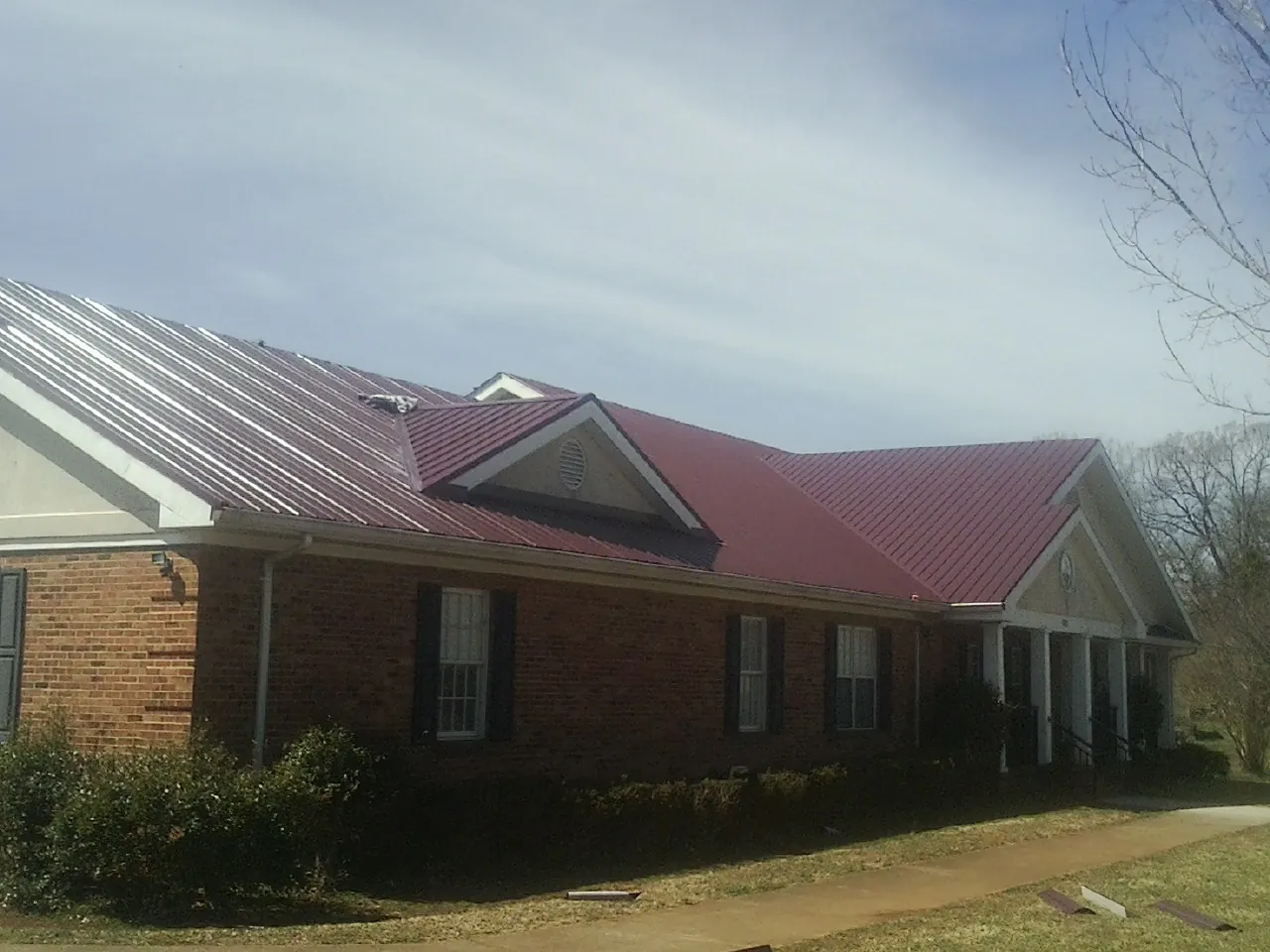 Red metal roof with gabled entries on a long brick building, from a Hail Damage Roof Repair job in Byron