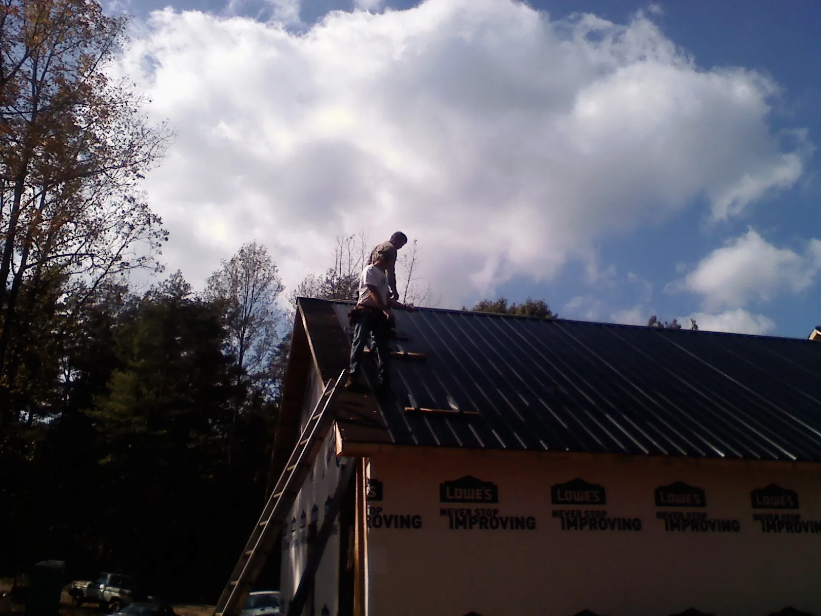 Roofer fastening dark metal panels high against a cloudy sky, from a Roof Inspection job in Byron